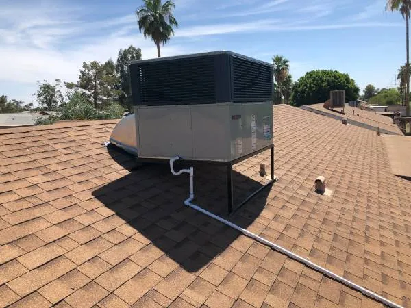 Package AC unit installed on a shingle roof with palm trees behind it