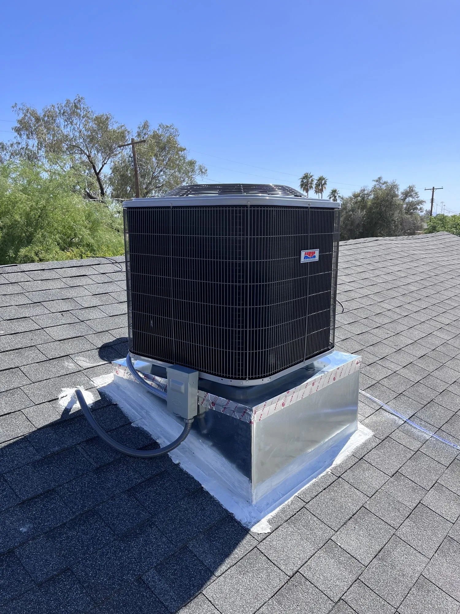 New Heil air conditioner installed on a Tucson shingle roof under a clear blue sky